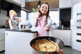 Cheerful siblings making crepes in the rustic home kitchen