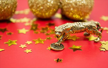 A bronze figure of a tiger with a coin - the symbol of the Chinese new year 2022 on a background of red, gold stars and balls, a copy space.