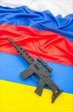 Russian and Ukrainian flags with black painted toy assault rifle. For Ukraine-Russia crisis, Russian invasion, tensions and war in Ukraine.