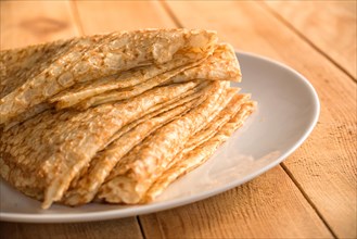 Close up on a stack of folded crepes (french pancakes) on a plate, wooden background