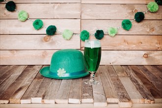 Glass of green beer with Irish festive hat on wooden background. Tabletop, side view.