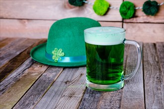 Mug of green beer with Irish festive hat on wooden background. Tabletop, front view.