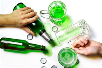 St. Patrick Day after party concept. Glasses and bottles of green beer on messy white table with beer caps