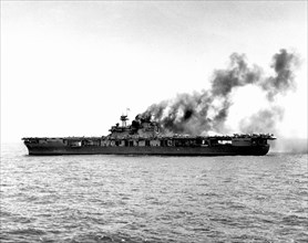 USS Yorktown (CV-5) dead in the water after being hit by Japanese bombs on 4 June 1942. The ship was hit shortly after noon. This view was taken about an hour later, with fires still burning in her up...