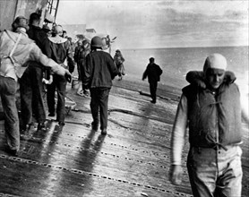 Scene on the flight deck of USS Yorktown (CV-5) shortly after she was hit by two Japanese aerial torpedoes, 4 June 1942. Men are balancing themselves on the listing deck as they prepare to abandon shi...