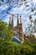 BARCELONA, SPAIN - MAY 13, 2017: The Sagrada Familia surrounded by trees and a beautiful blue sky, viewed from the Gaudi Square.