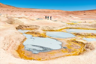Three tourists walking by the mud pits, fumaroles and geysers of Sol de Manana near the Uyuni salt flat (Salar de Uyuni) in the altiplano of Bolivia.