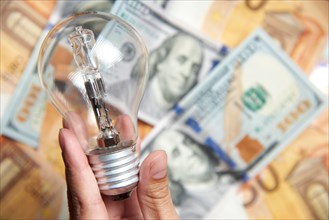 Female hand holding a light bulb on a background of banknotes. Concepts of energy efficiency, electricity expensive cost and power consumption.