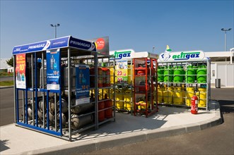 Household gas / gaz bottles in racks at supermarket garage, France.