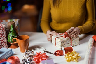 Woman wrapping Christmas gifts at home, she is tying a ribbon bow: holidays and celebrations concept