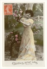 Early 1900's French sentimental tinted greetings postcard of a pretty woman in long flowing dress smiling and picking roses  - entitled "Picked for you", France, circa 1911