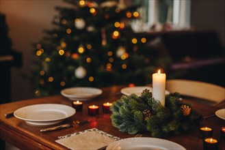Christmas candles in advent wreath with plates on dinner table. Scandinavian home decorated for Christmas dinner.