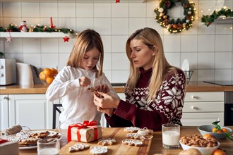 Mom helping kid daughter making Christmas cookies decorations at home.