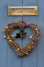 Christmas heart-shaped decoration hangs from festive red ribbon on a wooden door in the picturesque town of Ludlow, Shropshire, England, UK.