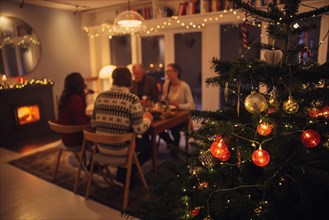 Interior shot of warm and cozy scandinavian home decorated for Christmas celebration. Focus on decorated Christmas tree with family sitting at dinner