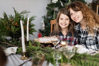 Family at Christmas at the festive table. Portrait of a happy mother and daughter at a decorated table in the living room. Candles, twigs