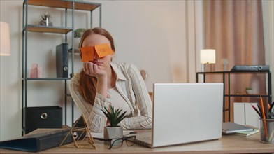 Tired woman teacher using laptop computer with funny stickers on eyes sleeps at workplace, napping