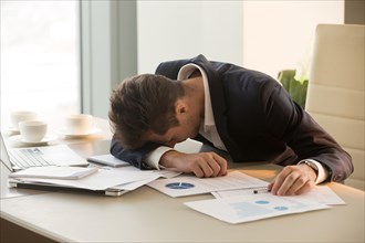 Tired young businessman sleeping on desk in office