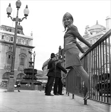 A model poses in a two piece skirt and jacket outdoors in London's Piccadillyby two patrolling policemen in circa 1968 wearing a colourful mini-dress.  Photo by Tony Henshaw