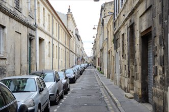 Many modern cars are parked at the side of the ancient narrow straight street in the French city Bordeaux.