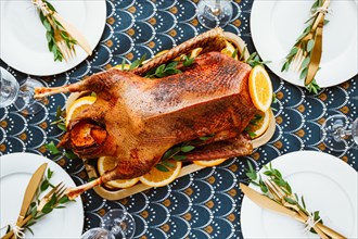 Festive table setting with whole roasted goose on a golden tray for celebrate event or Christmas family dinner. Top view, flat lay.