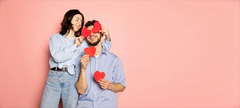 Flyer. Young and happy man and woman holding greeting cards shaped hearts isolated on pink trendy color background. Emotions, youth, love and