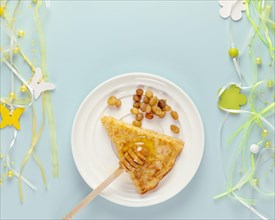 Homemade fried crepe with honey and raisins on a white plate with holiday decoration on a blue background with copy space. Russian national food. Chil