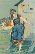 Postcard - vintage illustration of an Edwardian lady in bathing costume stepping into the sea from a bathing hut.