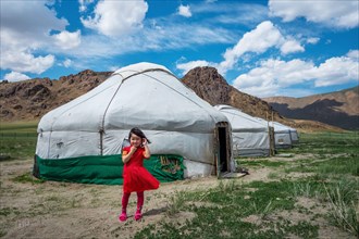 Mongolian girl in front of traditional yurts (Mongolian gers) on a sunny day in Bayan-Olgii, West Mongolia.
