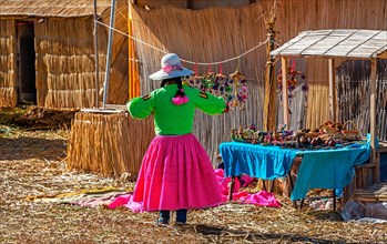 Indigenous art and craft saleswoman in flashy tribal colors on the Uros floating Islands with totora reed houses and floor, Titicaca Lake, Peru.