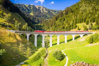 Bright sun over Glacier Express train traveling on Tujetsch viaduct in summer, Sedrun, Graubunden canton, Switzerland