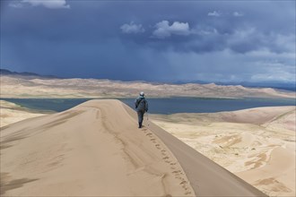 Tourist walking along the edge of the sand dune. Large barkhan in Mongolia sandy dune desert Mongol Els. Govi-Altay, Mongolia.