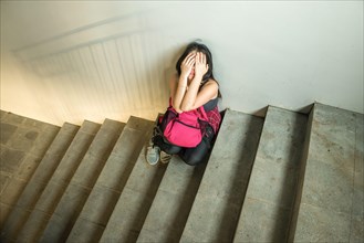young depressed and scared Asian Japanese student girl suffering abuse and harassment at school victim of bullying and discrimination sitting on colle