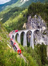 Rhaetian express moves on Landwasser Viaduct, Switzerland. This place is landmark of Swiss Alps. Vertical view of railroad bridge and red train, nice
