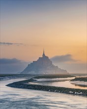 Moody sunrise at Le Mont Saint Michel abbey on the island in foggy morning, Normandy, Northern France, Europe. Popular travel destination