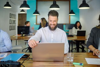 Cheerful man working on laptop in coworking space