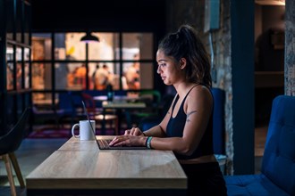 Female digital nomad working on laptop in contemporary coworking space