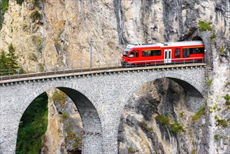 Bernina express glacier train on Landwasser Viaduct, Filisur, Switzerland. View of high railroad bridge and tunnel in rock of Swiss Alps. Theme of mou