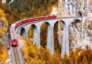 Bernina express glacier train on Landwasser Viaduct in autumn, Switzerland. Scenic view of railroad bridge in orange mountain forest in Swiss Alps. Th