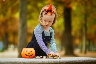 Adorable toddler girl in black cat dress with tutu skirt trick-or-treating with orange pumpkin bucket. Happy kid celebrating Halloween in Paris, Franc