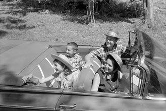 1960s FAMILY OF FOUR IN CONVERTIBLE LOOKING TOWARDS LEFT