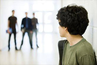 Teenage boy looking over shoulder at bullies in background