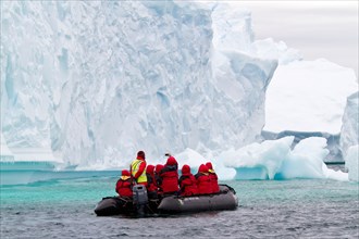 Antarctica cruise tourism with cruise ship passengers in zodiac boat viewing Antarctic glacier and iceberg, icebergs.