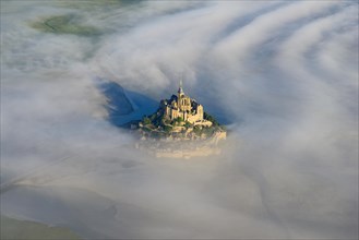 AERIAL VIEW. Abbey on an isolated peak above the morning fog. Mont Saint-Michel, Manche, Normandy, France.