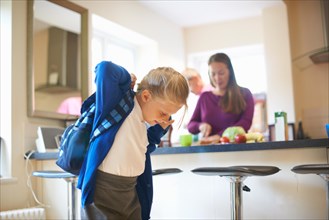 Schoolgirl putting on school satchel in kitchen