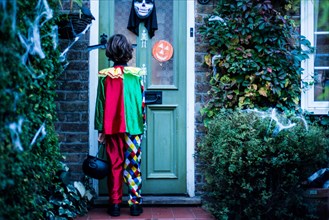 Young boy in halloween costume, standing at door, trick or treating, rear view