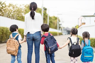 Mother and four kids holding hands are walking to school bus.Kids shoulder schoolbag.Back to school,primary school,Kindergarten,Group primary school