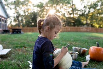 Side view of girl carving pumpkin while sitting in yard during Halloween
