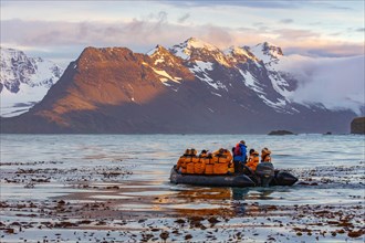 sunset on the snow capped mountains of the bay of isles in south Georgia in the foreground is a zodiac boat from an Antarctic cruise ship
