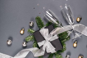 Christmas holiday composition. Black handmade gift boxes decorated with silver ribbon, tree branches, two glasses champagne confetti on gray backgroun